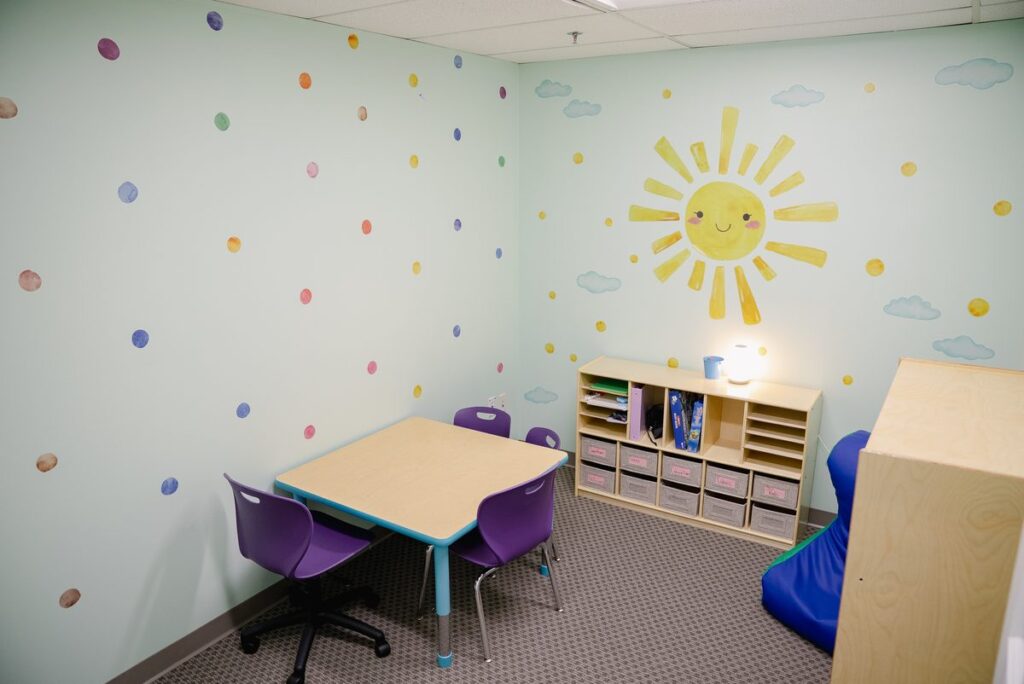 Therapy room with a sun mural, polka-dot walls and a small table at the Step It Up ABA Northlake center
