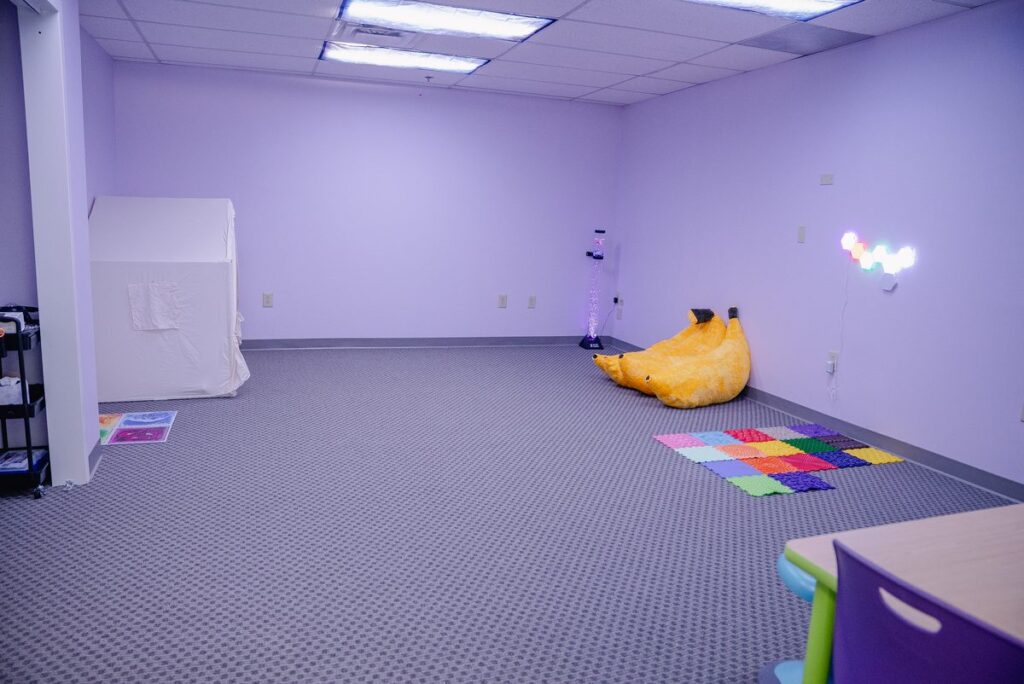 Purple sensory room with bean bags and a colorful floor mat at the Step It Up ABA Northlake center