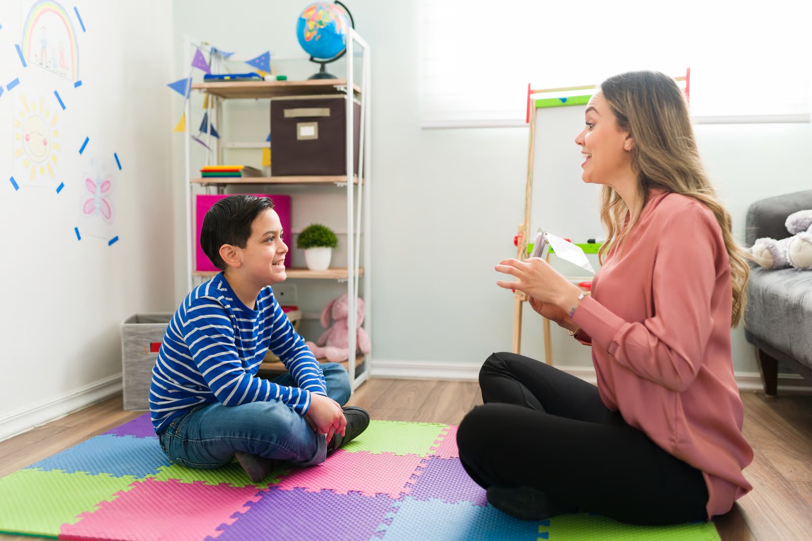 ABA therapist working with a smiling boy on a play mat at home