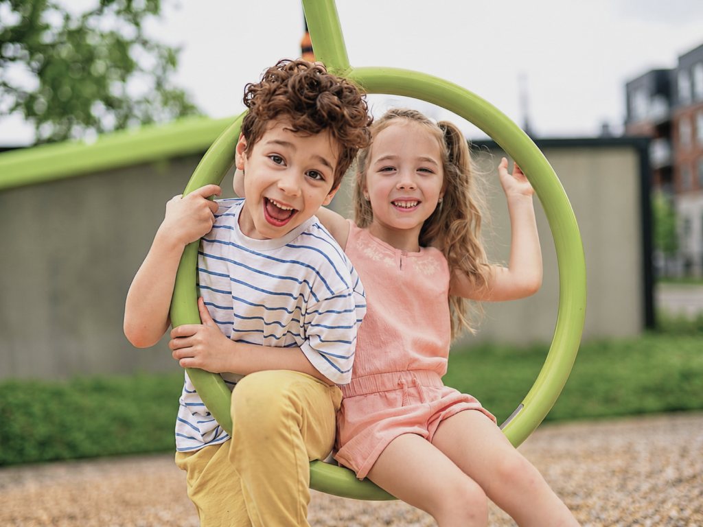 Two smiling children playing on a green ring at a playground